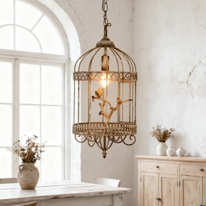 May include: A vintage-style birdcage pendant light fixture. The cage is made of distressed metal with a warm, aged finish. Inside, a decorative branch holds small bird figurines. The light fixture hangs from a chain and illuminates the room with a soft glow.