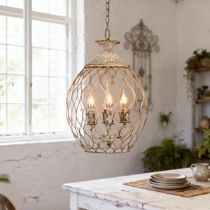 May include: A cream-coloured, antique-style chandelier with a woven metal cage design. The light fixture has three candelabra-style bulbs and hangs from a chain. The chandelier is suspended above a white table.
