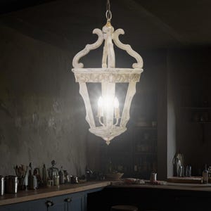 Op de afbeelding: Een witte houten kroonluchter met een lantaarnontwerp en vijf gloeilampen. De kroonluchter hangt aan het plafond in een kamer met een donkere achtergrond.