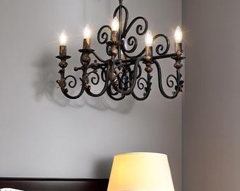May include: A black wrought iron chandelier with six lights. The chandelier has a scrolled design with a gold finish. The chandelier is hanging from a ceiling.