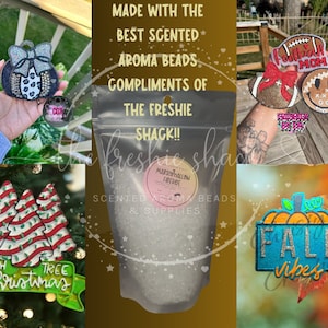 May include: Assortment of colorful, glittery, and felt ornaments with various themes, including Christmas, fall, and football. The ornaments are displayed on a wooden surface and a green tree branch. The text "MADE WITH THE BEST SCENTED AROMA BEADS COMPLIMENTS OF THE FRESHIE SHACK!!" is visible in the image.