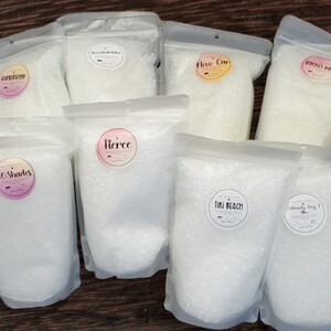 May include: Eight clear plastic bags filled with white bath salts. Each bag has a round label with a different scent name: "Barbershop", "Brown Sugar Vanilla", "New Car", "Rocket Pop", "50 Shades", "Fierce", "Tiki Beach", and "Deliciously Sangria".