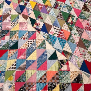 May include: A handmade quilt with a patchwork design. The quilt features a variety of fabrics in a geometric pattern of triangles. Colors include red, blue, green, yellow, and floral prints.