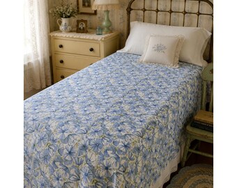 May include: A twin-sized bed featuring a white quilt with a repeating blue floral pattern. The bed includes a white pillow with a matching blue floral embroidery in the center, set against a metal headboard and a white lace-trimmed bed skirt.