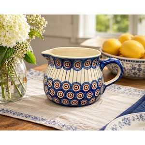 May include: A ceramic pitcher featuring a rounded body and a handle, decorated with a repeating pattern of blue and brown concentric circles on a cream background, with vertical blue lines connecting the circular motifs around the center.