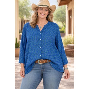 Peut inclure: Une femme porte un chemisier bleu à motifs, un jean bleu clair et un chapeau de cow-boy en paille. Le chemisier a un devant boutonné et des manches trois-quarts. Une ceinture marron avec une boucle décorative est portée à la taille.