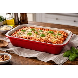 May include: A red rectangular baking dish filled with lasagna, topped with melted cheese and fresh basil leaves. The dish sits on a wooden surface with a white and gray striped cloth.