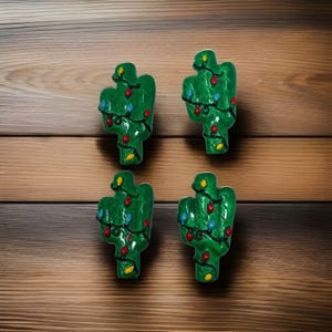 May include: Four green cactus-shaped ornaments decorated with colorful Christmas lights. The ornaments are arranged on a wooden surface. Each cactus has red, yellow, and blue lights, creating a festive holiday theme.