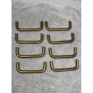 Puede incluir: Ocho tiradores de armario en tono latón dispuestos en dos filas de cuatro. Cada tirador tiene un diseño curvo y rectangular con un asa en forma de U. Los tiradores son de metal y tienen un cálido tono dorado.