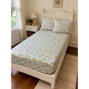 May include: A twin-sized bed frame features a white wooden headboard and footboard. The mattress is covered in a fitted sheet and two matching pillowcases, all decorated with a dense, colorful floral pattern in shades of yellow, blue, and pink.