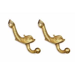 May include: Two gold-colored, fish-shaped hooks. The hooks have a curved design with a fish head and tail, and a ball at the end of the hook. The hooks are made of metal and are likely for decorative or functional use.