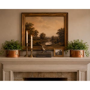 May include: Two hammered copper planters with leaf accents, two brass candlesticks with white taper candles, a small bird figurine, two stacked books titled The Country House and A Year in Our Garden, and a framed landscape painting.