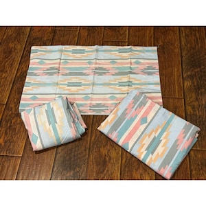 May include: A bedding set consisting of a flat sheet and two pillowcases, all featuring a repeating geometric pattern in soft shades of light blue, pale pink, cream, and grey. The fabric displays horizontal bands of diamonds and stripes.