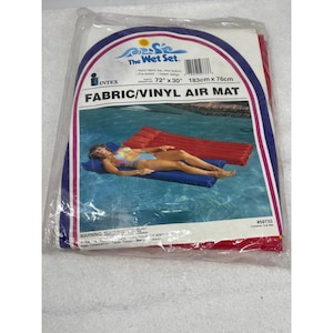 May include: A packaged Fabric/Vinyl Air Mat from The Wet Set. The package features a blue, red, and white design with the text "72" x 30"" and "183cm x 76cm". The image on the package shows a person relaxing on a blue air mat in a pool.