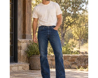 Puede incluir: Una camiseta de manga corta color crema con bolsillo en el pecho, combinada con pantalones vaqueros azul oscuro y botas de cuero marrón. Una gorra de béisbol bicolor con visera oscura y corona clara completa el conjunto informal.