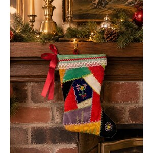 May include: A patchwork Christmas stocking featuring various fabric textures and colors including red, green, yellow, and blue. The stocking is adorned with intricate embroidery of flowers and a star, finished with a white lace trim and a red ribbon bow.