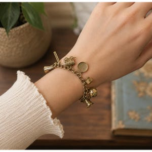 May include: A gold-toned metal charm bracelet featuring various cinema-themed charms, including a film projector, a megaphone, a film strip, a round frame, a small box, and a bell, all attached to a classic link chain with a secure clasp.