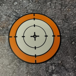 Pode incluir: Um alvo redondo laranja e branco com um centro preto e uma mira.