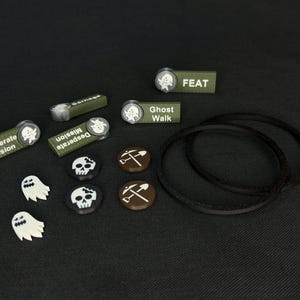 Pode incluir: Um conjunto de peças de jogo para um jogo de RPG de mesa. As peças incluem uma variedade de fichas, como crânios, fantasmas e uma picareta. Há também vários cartões retangulares verdes com texto branco, incluindo "Missão Desesperada", "Caminhada Fantasma" e "Proeza".