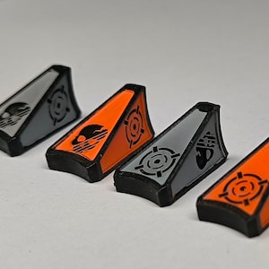 Può includere: Quattro piccoli pezzi di plastica a forma triangolare con una base nera e una metà superiore arancione o grigia. Ogni pezzo ha un design nero di teschio e ossa incrociate e un design di bersaglio nero.