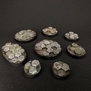 May include: A set of eight round and oval-shaped miniature bases for tabletop gaming. The bases are made of a textured, gray material with a stone-like appearance.