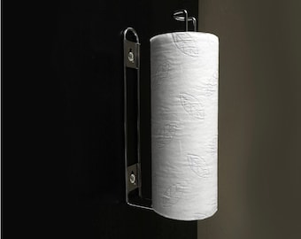 May include: A wall-mounted paper towel holder made of stainless steel. It features a vertical bar with screws and a curved top to hold the paper towel roll. The white paper towel roll has a leaf pattern.