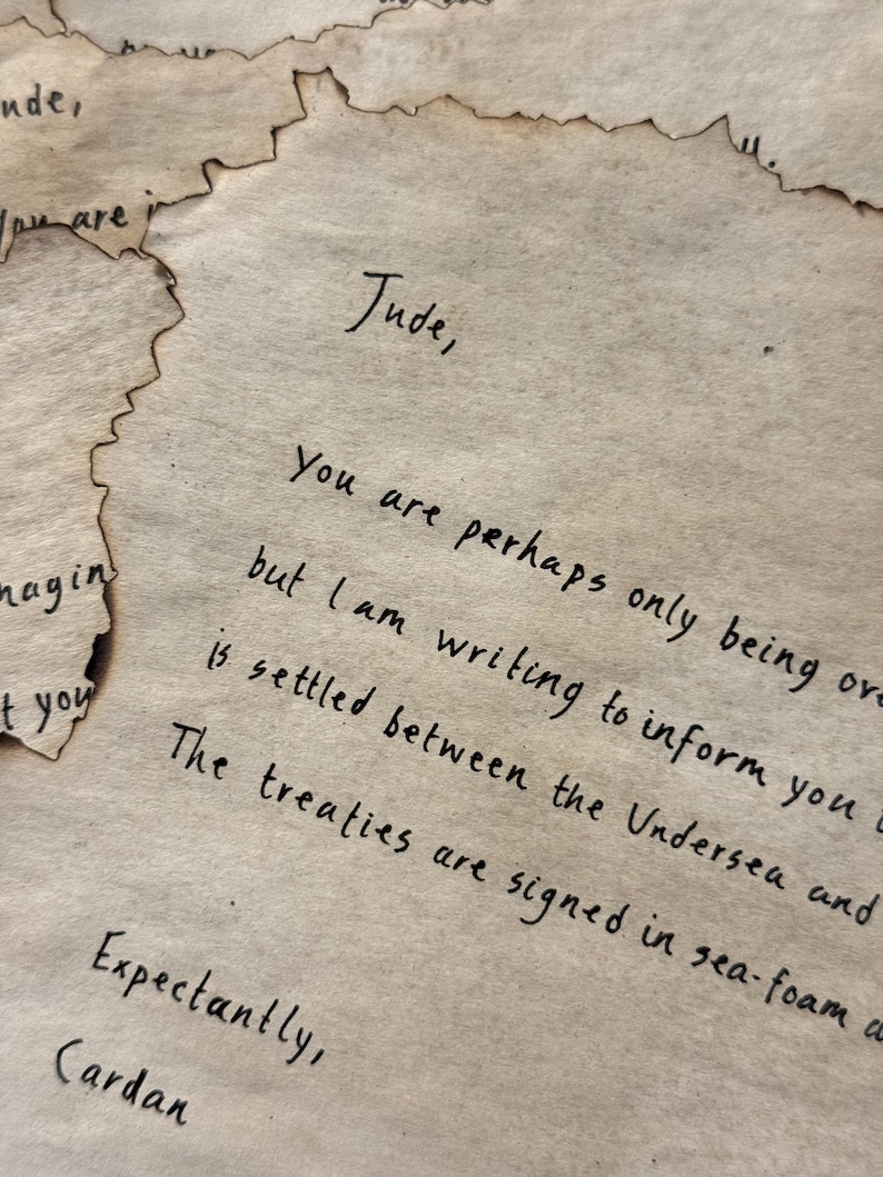 May include: Aged parchment paper with handwritten text. The letter is addressed to "Jude" and signed "Cardan." The edges of the paper are torn and singed, giving it an antique appearance. The text is in black ink.