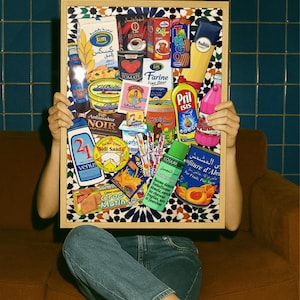 Peut inclure: Un collage encadré de divers emballages de produits alimentaires, dont du café et de la farine. Le collage est tenu par une personne portant un jean bleu et des chaussures blanches. Le fond présente un mur carrelé bleu et un canapé marron.