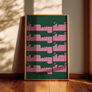 May include: A framed art print with a gold border. The artwork features repeating pink Arabic calligraphy on a dark green background. The print is leaning against a wall on a wooden floor.