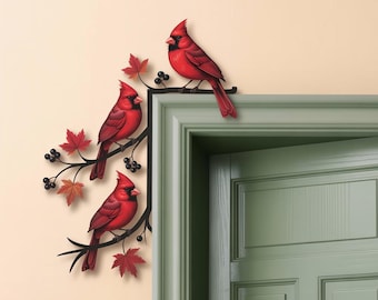 May include: A decorative metal wall art piece featuring three vibrant red cardinal birds perched on a black branch with red maple leaves and black berries. The artwork is mounted on a beige wall near a green door frame.