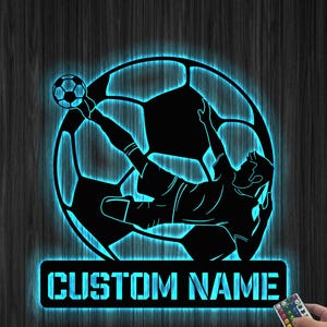 May include: A blue and black silhouette of a soccer player kicking a ball with the text "CUSTOM NAME" below. The image is a night light with a remote control.