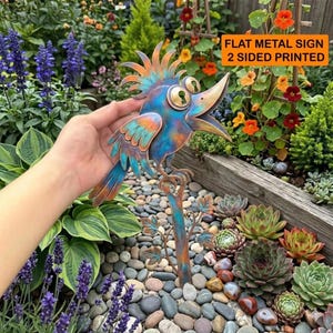 May include: A flat metal sign shaped like a bird with a crest, featuring a blue and copper patina finish, large eyes with keyhole pupils, and an open beak. The sign is two-sided and printed with a stylized bird design on a metal stake.