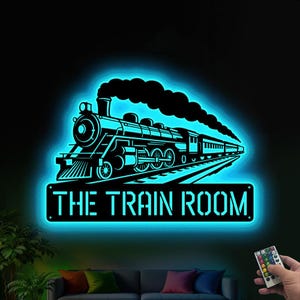 May include: Black metal train sign with a blue neon glow. The sign features a detailed train silhouette with the text "THE TRAIN ROOM" below. The image is illuminated with a blue light, creating a striking visual effect.