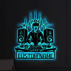 Puede incluir: Un letrero de neón negro y azul que representa a un DJ con auriculares, tocadiscos y altavoces. El letrero incluye un gráfico de onda de sonido y el texto "CUSTOM NAME" en un marco rectangular. Montado en una pared oscura y texturizada.