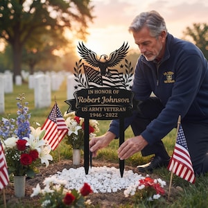 May include: A black metal memorial garden stake featuring a laser-cut eagle perched atop an American flag. The plaque displays the text IN HONOR OF Robert Johnson, US ARMY VETERAN, and the years 1946-2022, supported by two pointed stakes.