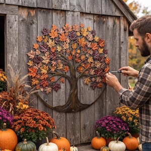 Puede incluir: Una pieza de arte mural circular de metal que presenta un árbol con numerosas hojas de arce en tonos naranja, rojo y amarillo. La escultura tiene un tronco y ramas de color marrón oscuro y está montada sobre una pared de madera.