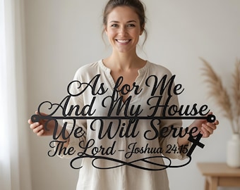 May include: Black metal wall art with the quote "As for Me And My House We Will Serve The Lord - Joshua 24:15". The sign has a decorative scroll design and a cross. The art is held by a person.