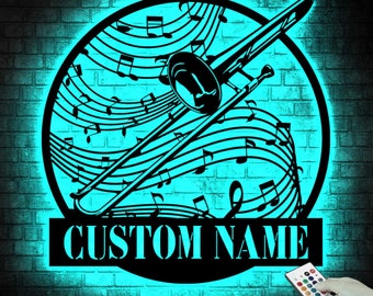 May include: A black trombone silhouette with musical notes and staff lines, set within a circular frame. The words "CUSTOM NAME" are displayed below. The background is a brick wall illuminated with a turquoise glow. A remote control is in the lower right corner.