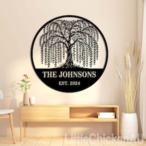 May include: A black metal family name sign featuring a detailed weeping willow tree design within a circular frame. The text "THE JOHNSONS" and "EST. 2024" are displayed below the tree. The sign is mounted on a wall above a wooden cabinet.