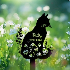 Könnte beinhalten: Schwarze Metallsilhouette einer Katze, die mit Blumen sitzt und den Text "Kitty 2012-2024" trägt.