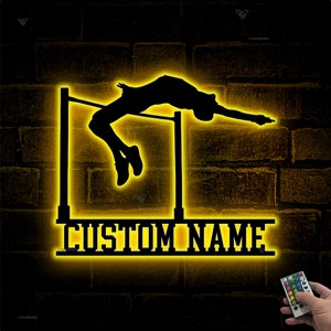 Puede incluir: Una silueta negra de un saltador de altura que supera una barra, iluminada con un brillo amarillo. Las palabras "CUSTOM NAME" están debajo del saltador. El fondo es una pared de ladrillos oscuros.