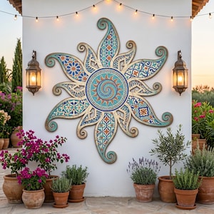 May include: A large, decorative sunburst wall hanging with a mosaic design in shades of blue, turquoise, and orange. The sunburst is mounted on a white wall, with two lanterns and potted plants in the foreground. The overall theme is Mediterranean decor.