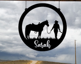 May include: Black metal circular sign featuring a horse and rider silhouette within a circle. The sign is suspended by chains from a wooden beam. The name "Sarah" is written in cursive below the horse and rider.