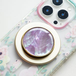 Könnte beinhalten: Eine goldene Handyhülle mit Blumenmuster und einem rosa und goldenen PopSocket mit einem perlmuttartigen, schillernden Zentrum.
