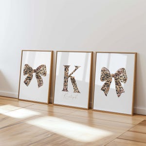 May include: Three framed prints with a gold border. Two prints feature a bow with a leopard print design. The center print displays the letter "K" in a leopard print pattern with the name "Kristoph" below.