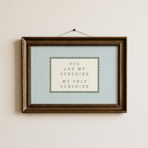 Puede incluir: Un cuadro enmarcado con la frase "YOU ARE MY SUNSHINE MY ONLY SUNSHINE". El fondo es de rayas azules y blancas, y el marco es de color marrón.