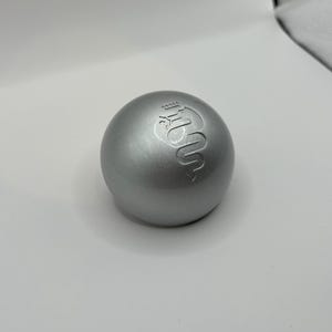 May include: A silver-colored sphere with a raised logo of a snake with a crown on its head.