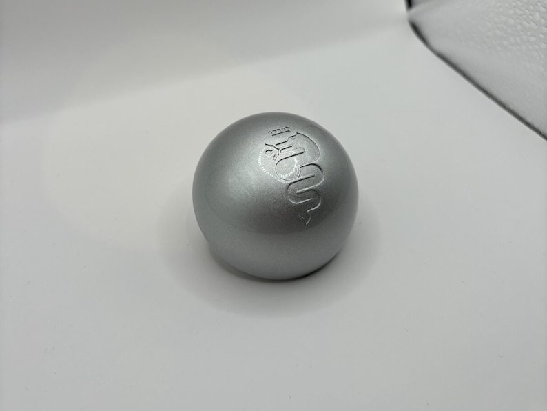 May include: A silver-colored sphere with a raised logo of a snake with a crown on its head.