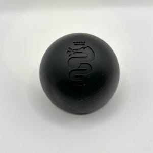 May include: A black round gear shift knob with a silver Alfa Romeo logo.