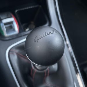 Può includere: Un pomello del cambio in pelle nera con la scritta "Giulietta" in rilievo.